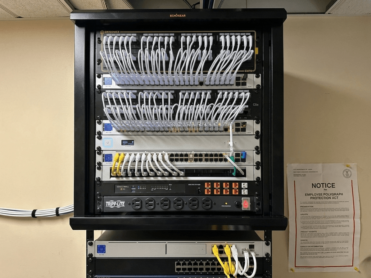 The same network closet after cleanup - enclosed wall rack with dressed white patch cables