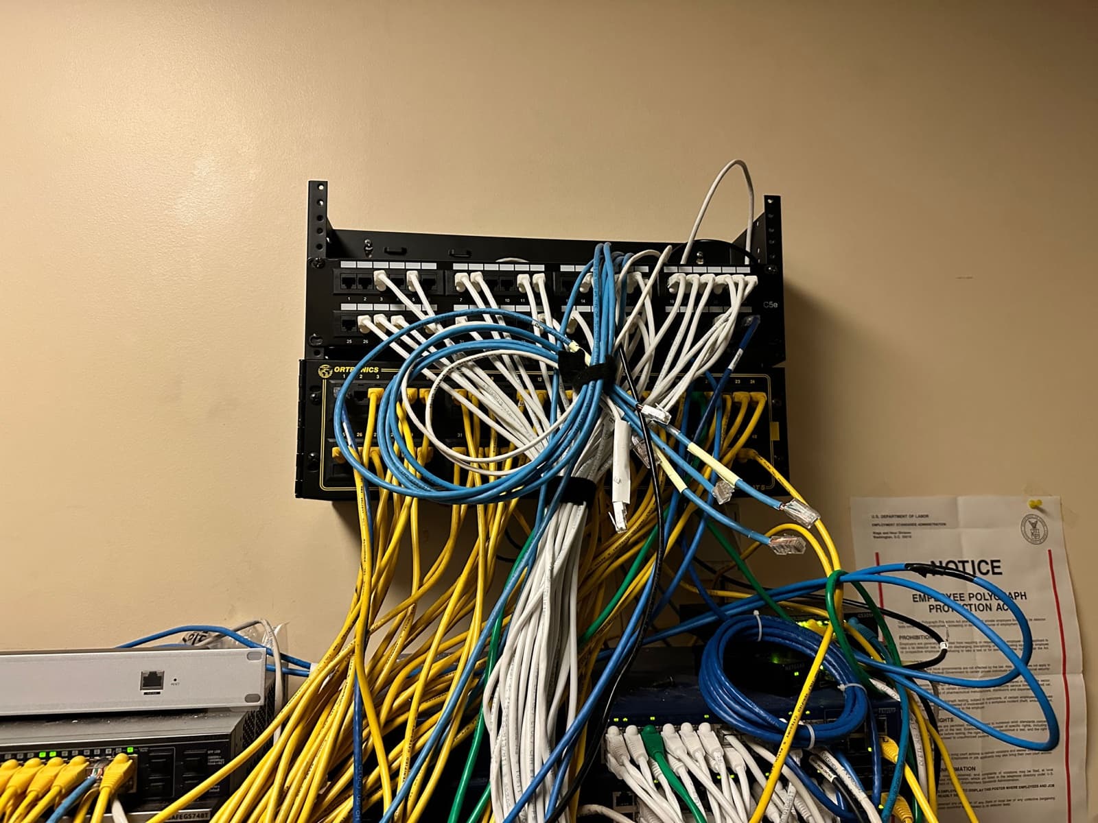 Wall-mounted patch panels buried under a tangle of unlabeled yellow, white, and blue cables